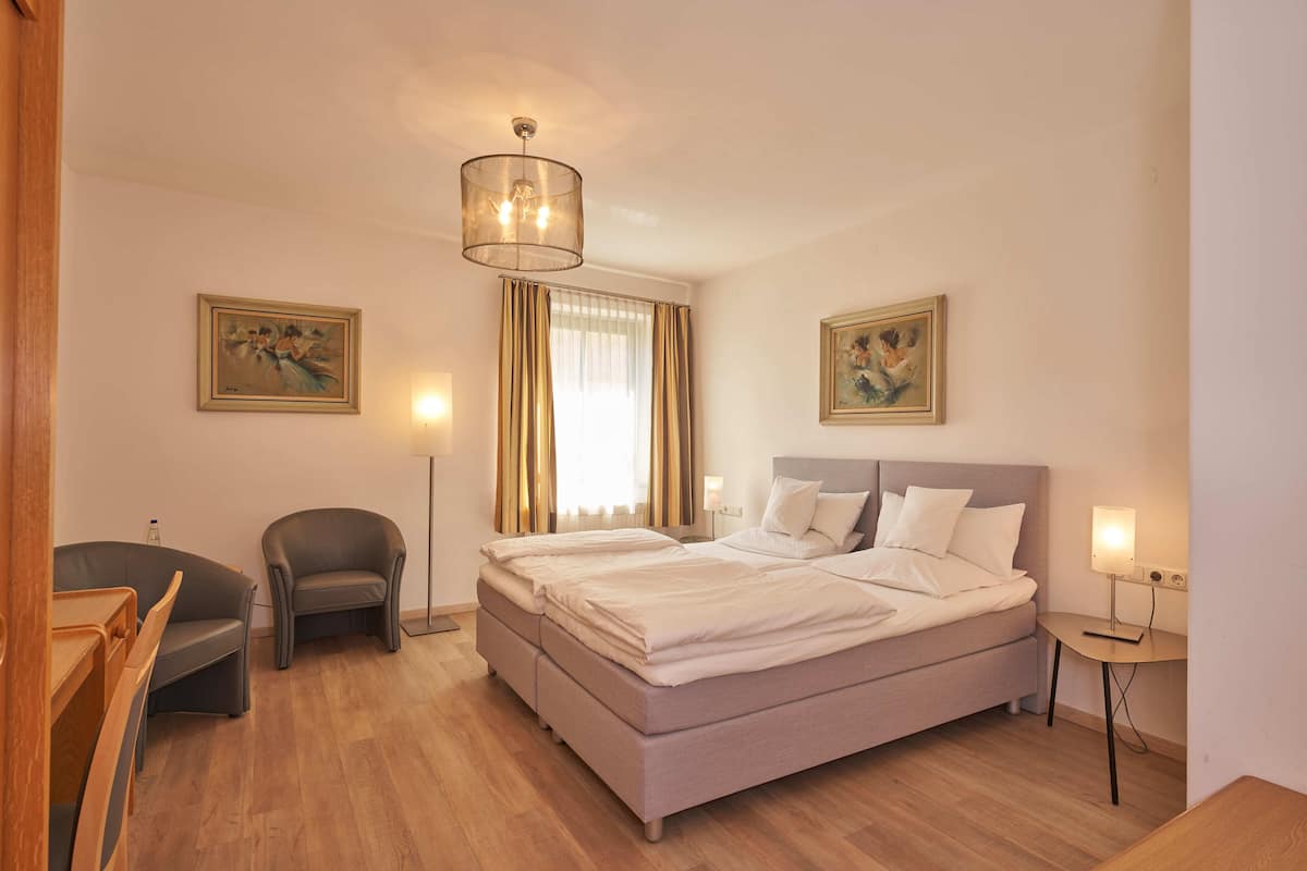 A hotel room with a bed, a desk, a chair, and two paintings on the walls.