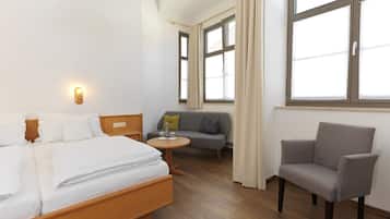 Une chambre d’hôtel avec un lit, un canapé, une chaise, une petite table et une fenêtre avec des rideaux.