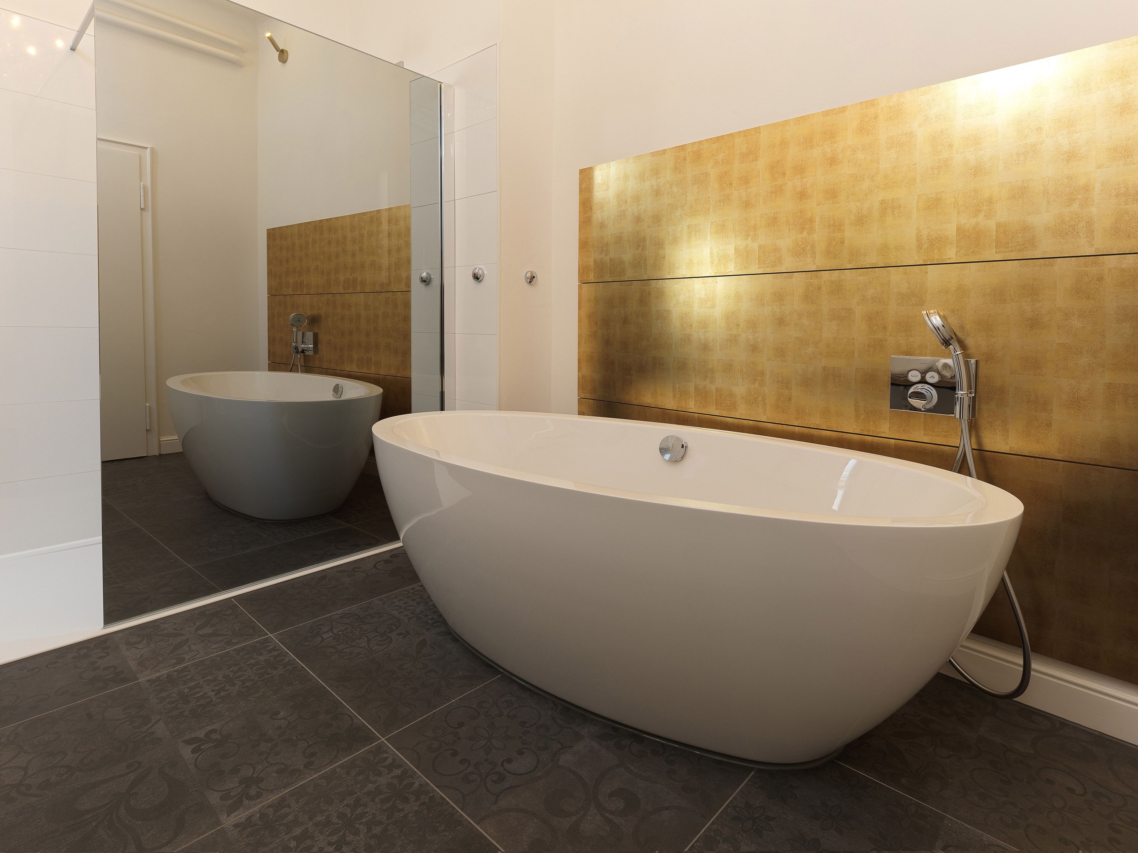 Un baño moderno con una bañera independiente, un lavamanos separado y un espejo grande.
