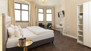 A modern hotel room with a large bed, a desk, a chair, a TV, and a minibar. - Lodner Genießerhotel Drei Mohren (Lauingen)