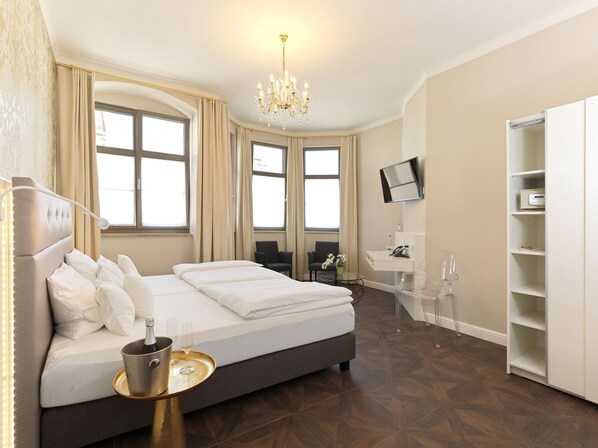 A modern hotel room with a large bed, a desk, a chair, a TV, and a minibar.