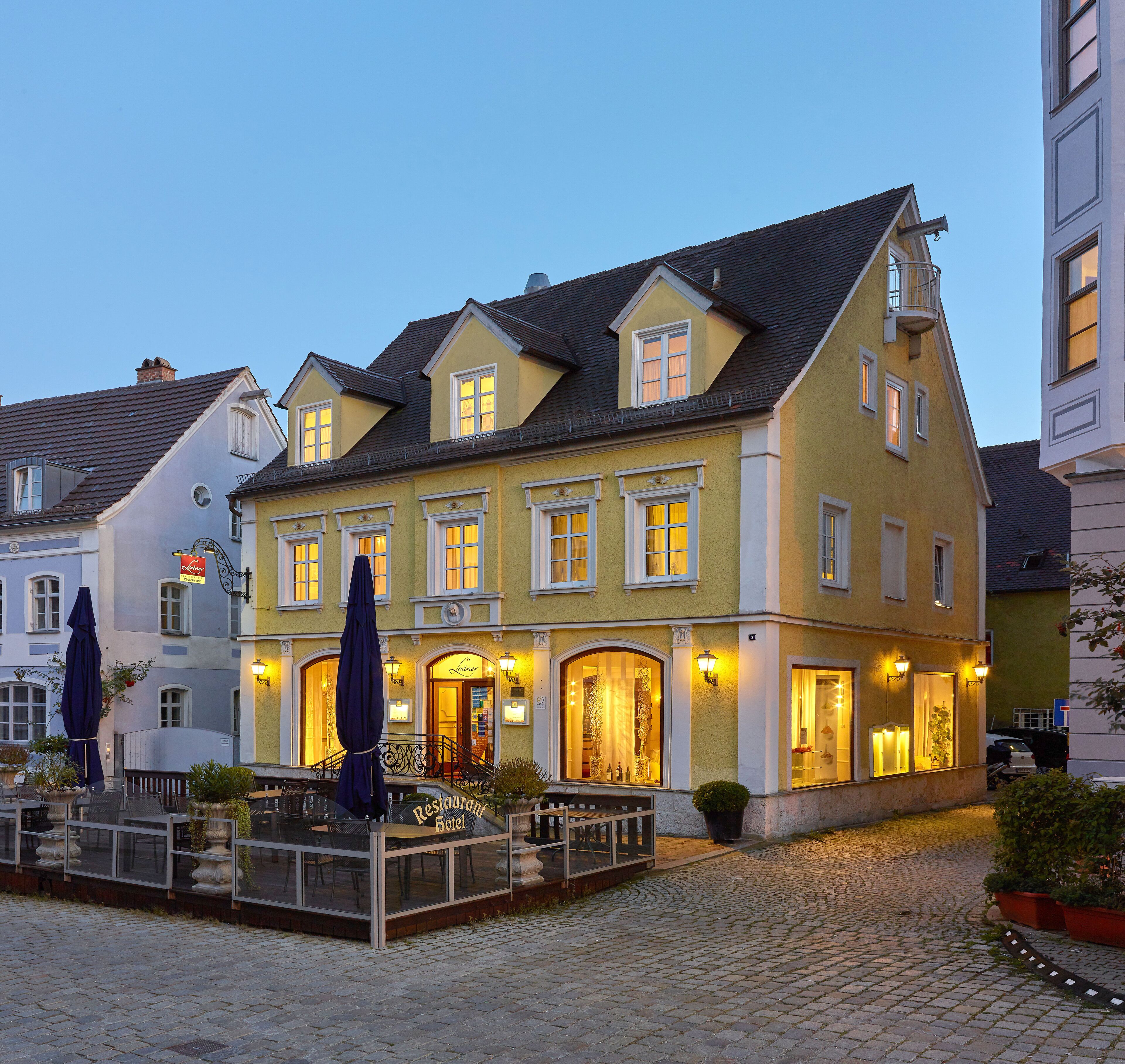 A traditional European hotel with a courtyard, outdoor seating, and a well-lit entrance.