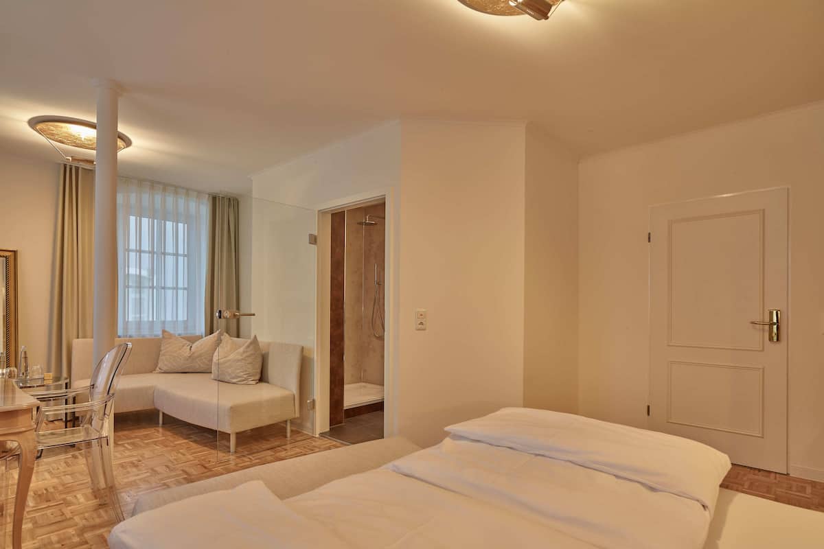A hotel room with a bed, a sofa, a chair, a desk, and a shower area.