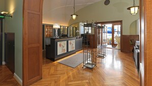 A hotel lobby with a wooden reception desk, a large mirror, and a seating area with a view of the outdoors. - Lodner Genießerhotel Drei Mohren (Lauingen)