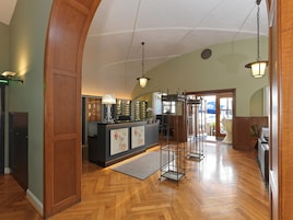 A hotel lobby with a wooden reception desk, a large mirror, and a seating area with a view of the outdoors.