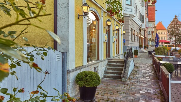 A hotel with a yellow facade, a staircase leading to the entrance, and a tower in the background. - Lodner Genießerhotel Drei Mohren (Lauingen)