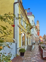 A hotel with a yellow facade, a staircase leading to the entrance, and a tower in the background.