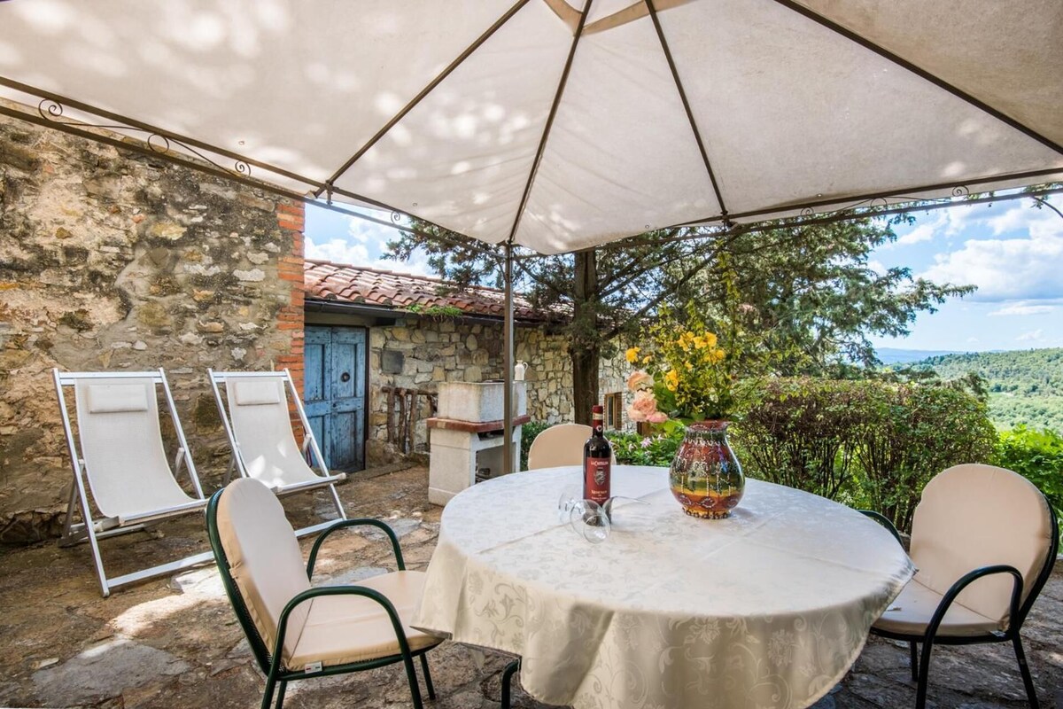 An outdoor patio with a round table, chairs, a bottle of wine, and a vase of flowers.