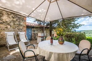 Une terrasse extérieure avec une table ronde, des chaises, une bouteille de vin et un vase de fleurs.
