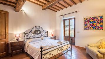 A bedroom with a bed, nightstands, a wooden door, a window, and a colorful wall decoration.
