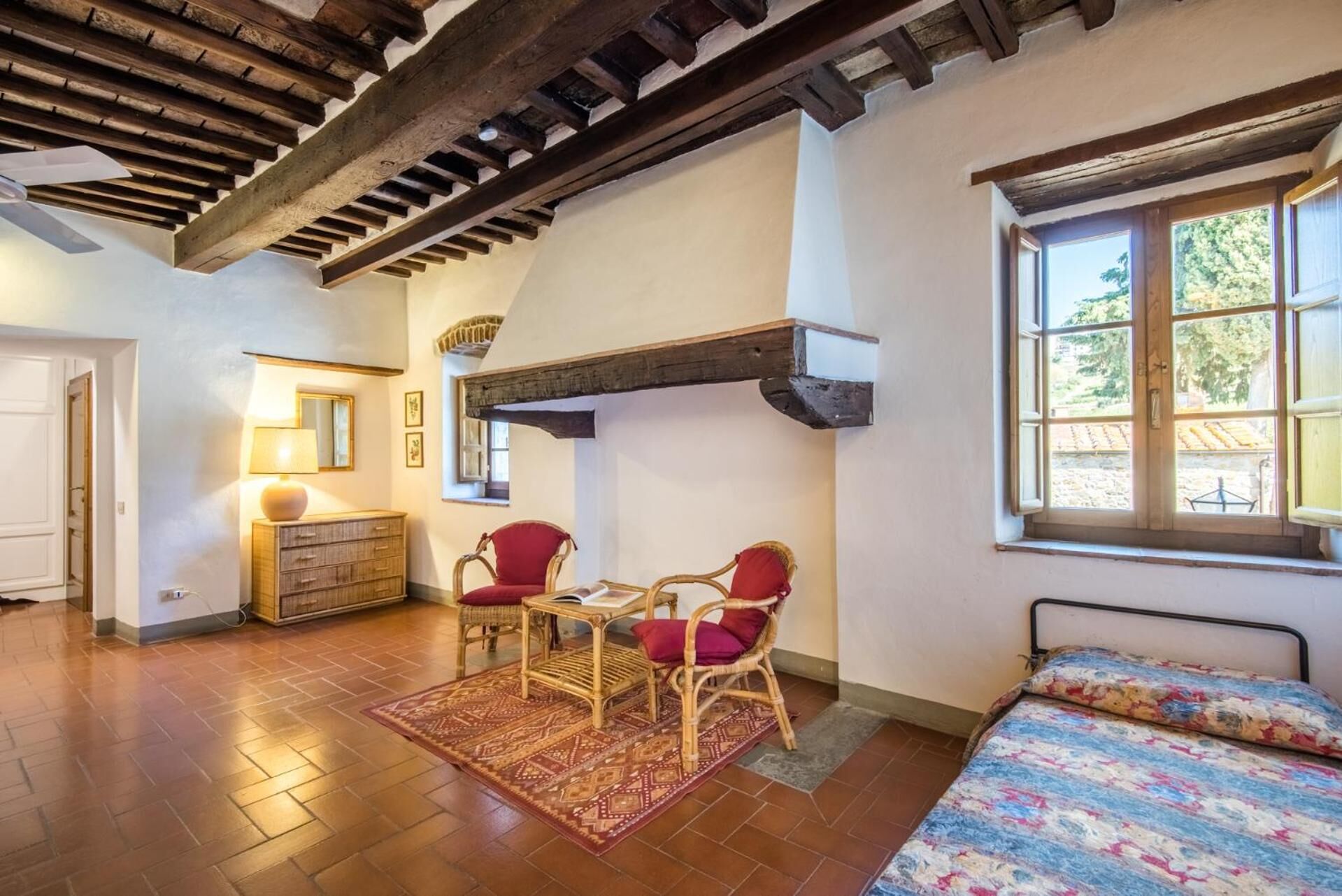 A cozy room with a wooden ceiling, a bed with a floral bedspread, a red chair, a wooden dresser, and a table with chairs.
