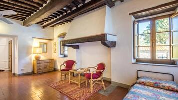 A cozy room with a wooden ceiling, a bed with a floral bedspread, a red chair, a wooden dresser, and a table with chairs.