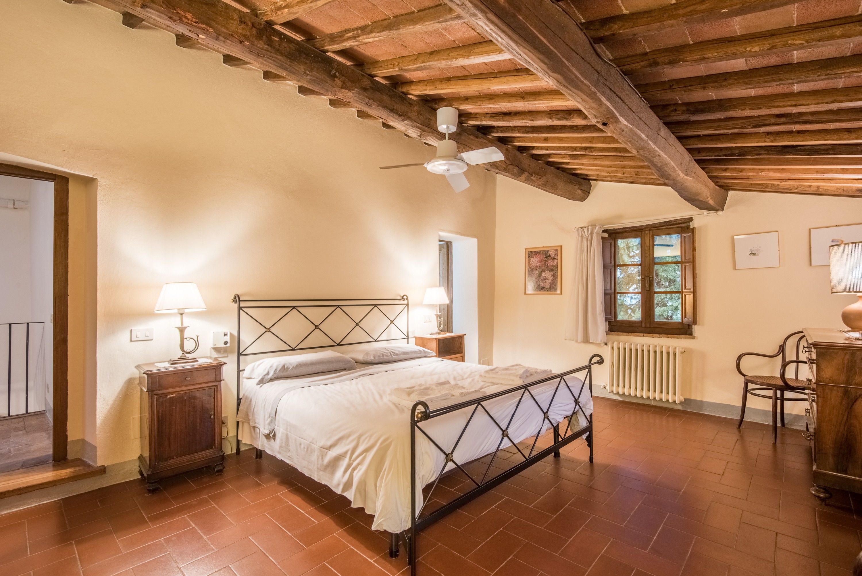Une chambre à coucher comprenant un lit, des tables de chevet, un radiateur, une fenêtre et un ventilateur de plafond.