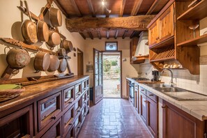 A rustic kitchen with wooden cabinets, a stone floor, and hanging pots.