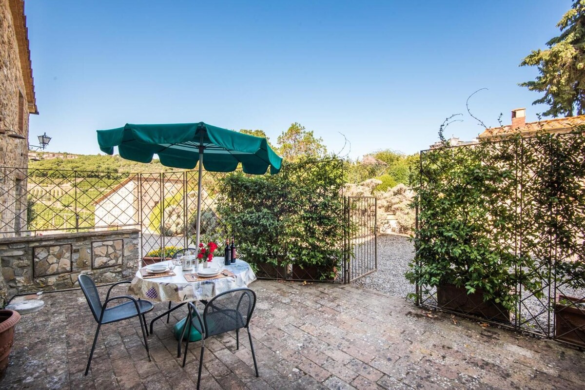 An outdoor patio with a table set for two, surrounded by stone walls and greenery.