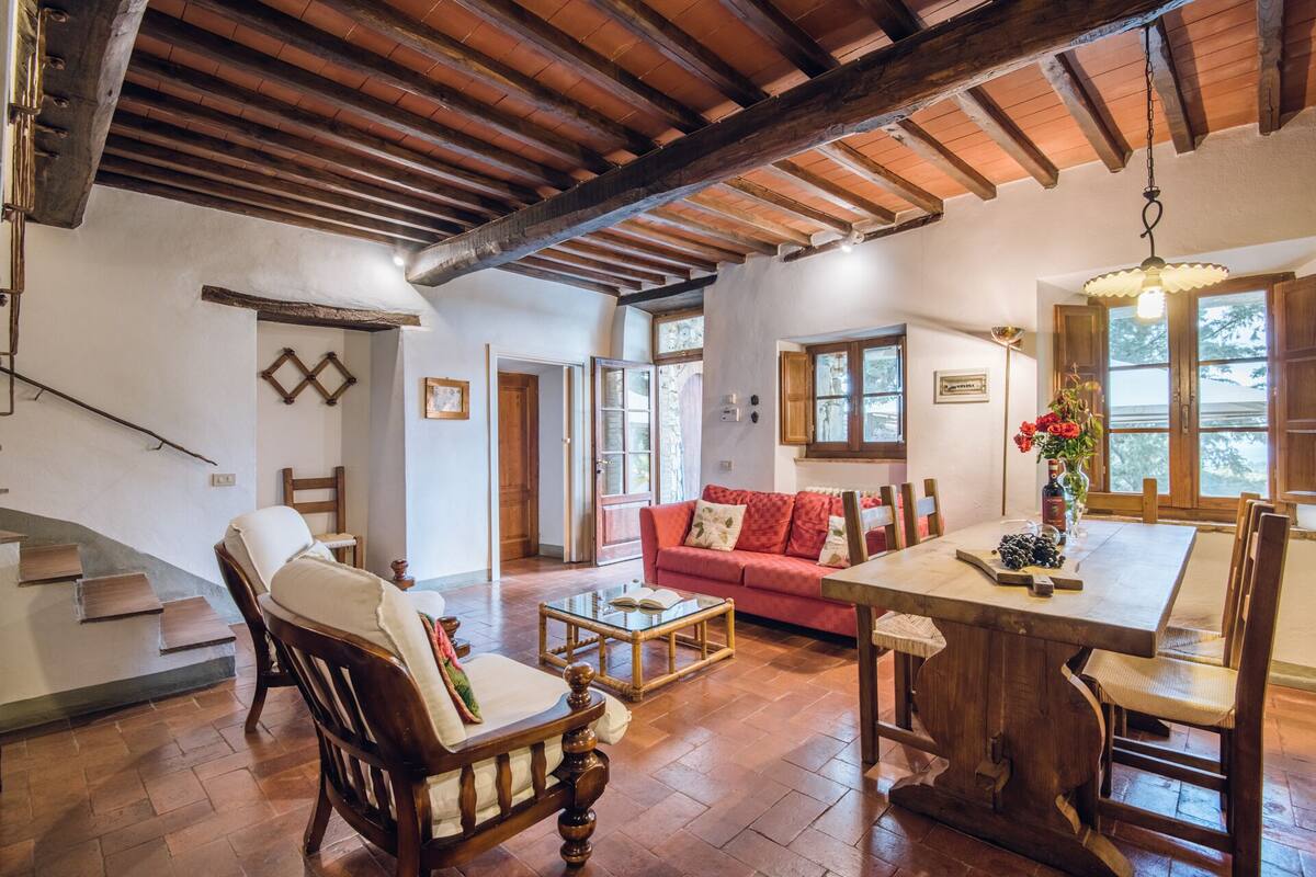 Un salón amplio con techo de madera, un sofá rojo, una mesa de comedor de madera y una escalera que sube a otra habitación.