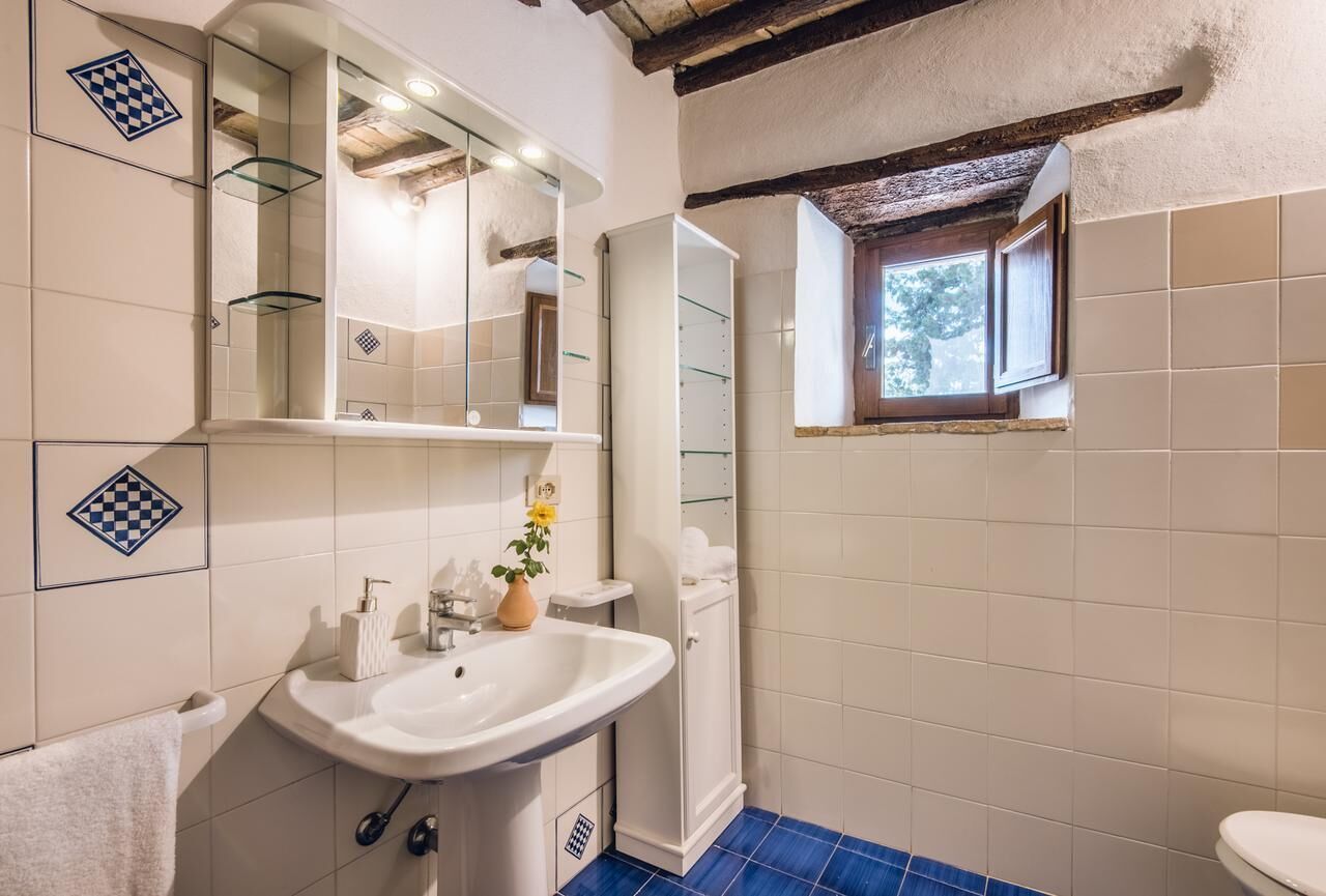 A bathroom with a white sink, a mirror, a towel rack, and a window with a view of trees.