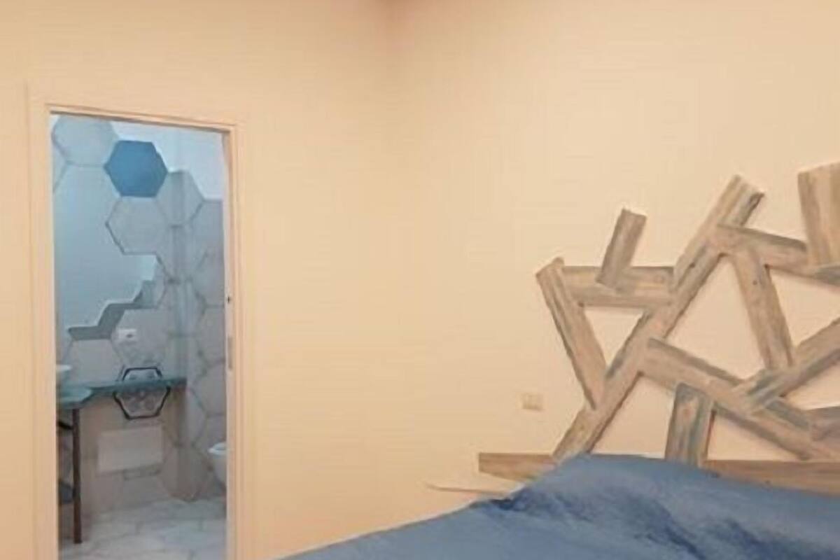 A bedroom with a bed, a wooden wall art piece, and a bathroom visible through a glass door.