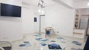 A modern kitchen with a flat-screen TV, a dining table with chairs, and a patterned floor. - I Colori del Mare (Milazzo)