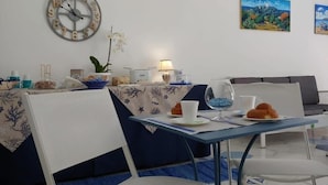 A dining area with a table set for two, a clock on the wall, and two paintings. - I Colori del Mare (Milazzo)