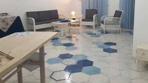 A living room with a sofa, two armchairs, a coffee table, and a dining table. The room has a patterned floor and a ceiling light fixture. - I Colori del Mare (Milazzo)