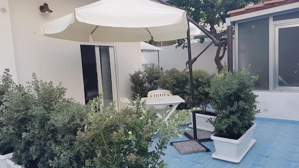 A small patio area with a white umbrella, a white chair, and potted plants. - I Colori del Mare (Milazzo)