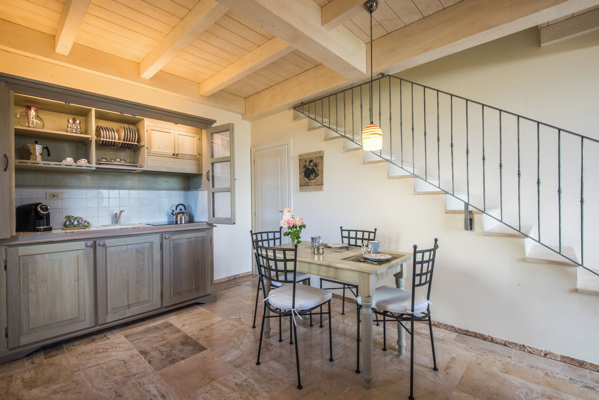 A kitchen with wooden cabinets, a dining table with chairs, and a staircase with a metal railing.