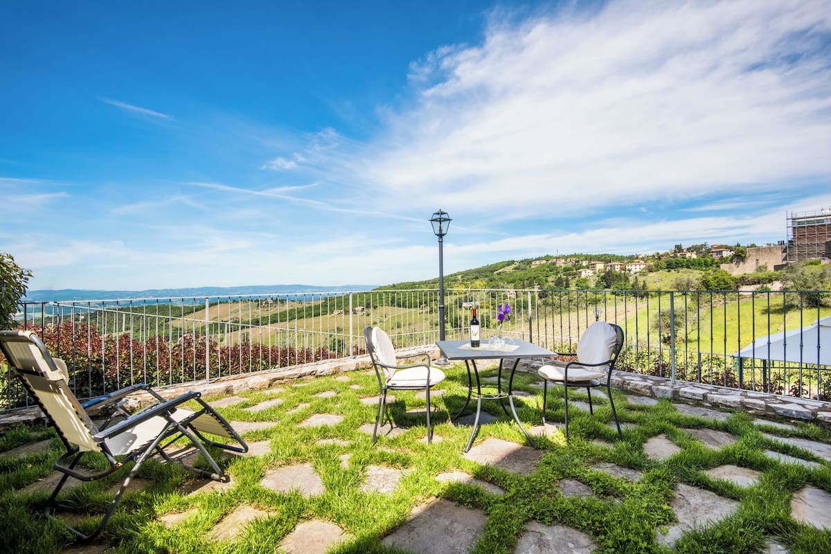 Une terrasse avec un sol en pierre, une table et des chaises, et une vue sur un paysage vallonné.