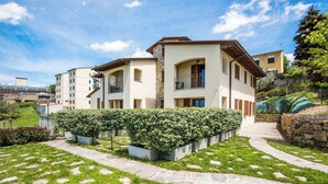 A modern two-story residential building with a stone facade, a well-maintained garden with hedges and grass, and a clear sky. - Casa Vacanze Squarcialupi (Castellina in Chianti)