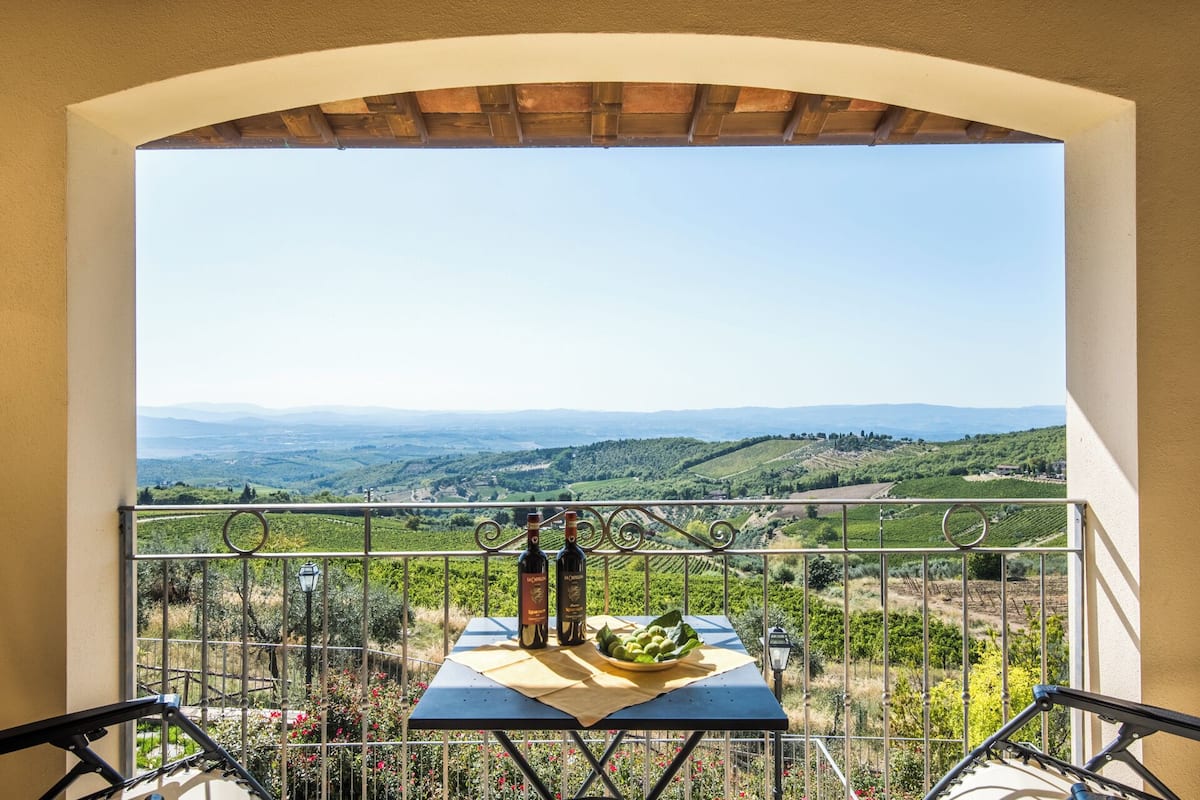 Un balcon avec une table dressée pour deux personnes, d’où l’on peut admirer un vignoble et des collines lointaines.