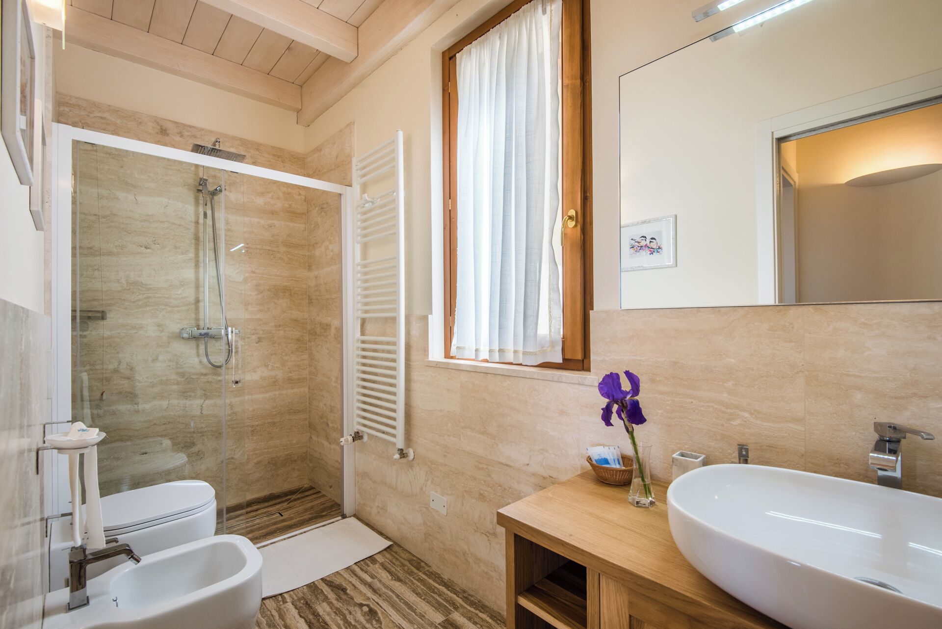 A bathroom with a glass-enclosed shower, a toilet, a sink, and a window with white curtains.