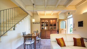A dining area with a wooden table and chairs, a white sofa with cushions, and a staircase with a metal railing. - Casa Vacanze Squarcialupi (Castellina in Chianti)