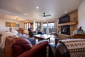 A cozy living room with leather furniture, a fireplace, and a large window offering a mountain view.