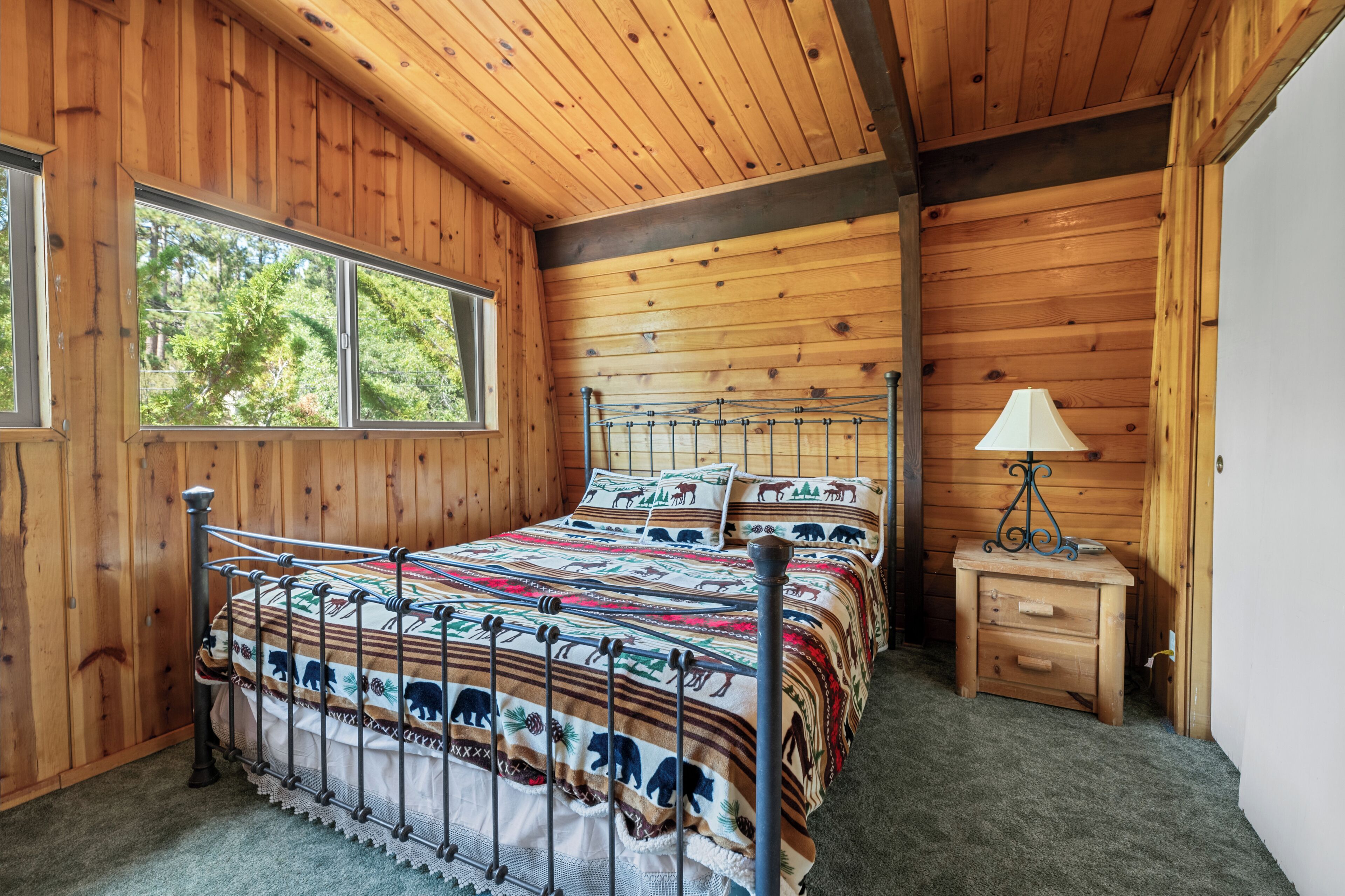 Een slaapkamer in een houten blokhut met een bed, een nachtkastje en een raam.
