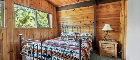 Een slaapkamer in een houten blokhut met een bed, een nachtkastje en een raam.