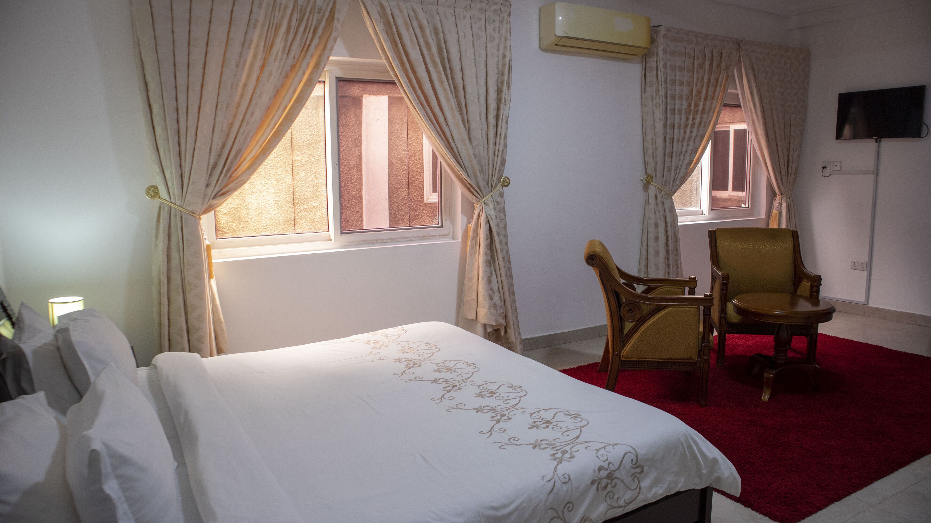 A hotel room with a bed, a chair, and two windows with curtains.