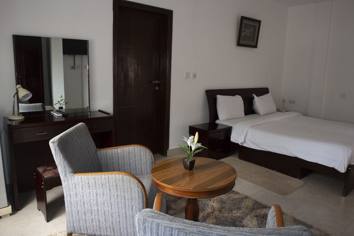 Une chambre d’hôtel comprenant un lit, un bureau avec une chaise, une table ronde avec un vase et un grand miroir.