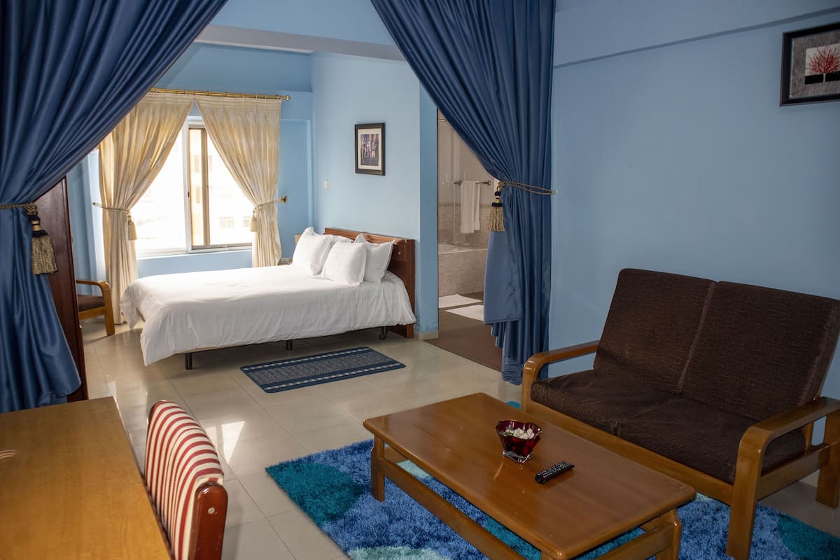 Une chambre d’hôtel comprenant un lit, un canapé, une table basse et une salle de bain visible à travers une porte en verre.