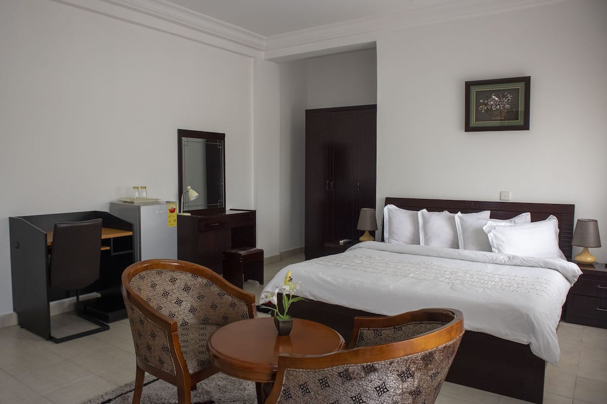 Une chambre d’hôtel comprenant un lit, un bureau, une chaise, une petite table, un miroir, une armoire et un tableau encadré au mur.