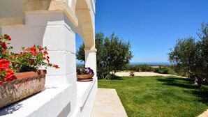 A white building with a stone pathway leading to a grassy area with potted plants and a view of the sea. - Masseria Spetterrata (Fasano)