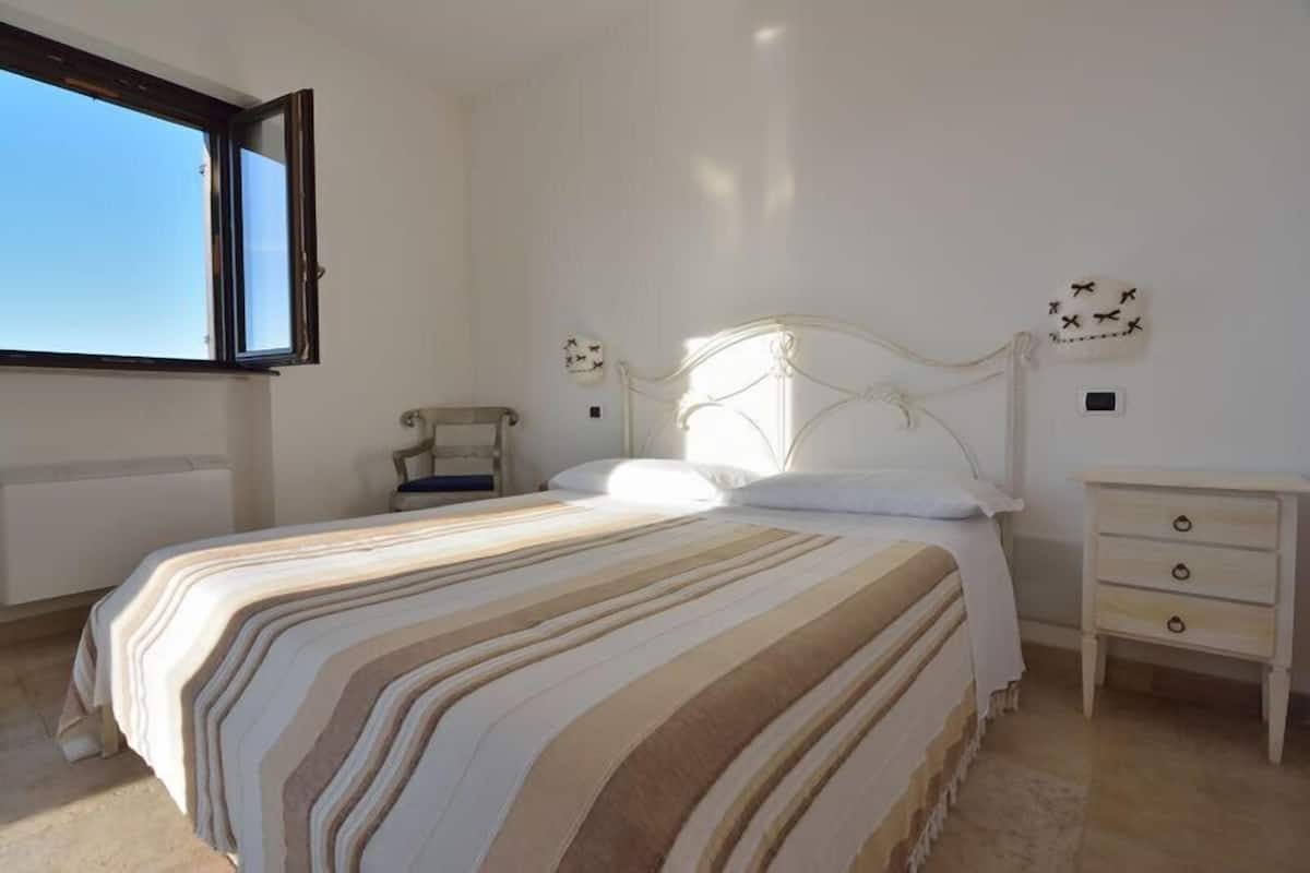 A bedroom with a bed, a nightstand, a chair, and a window.
