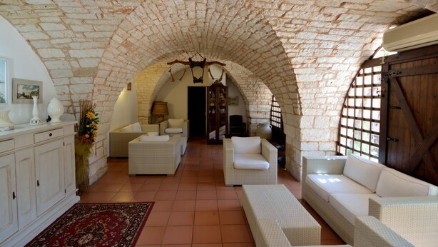 A spacious living room with a high stone ceiling, white wicker furniture, and a red rug. - Masseria Spetterrata (Fasano)