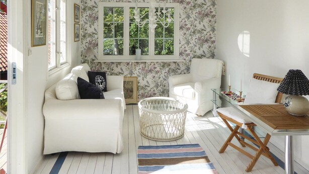 Una habitación acogedora con un sofá blanco, una cesta de mimbre, una mesa de madera y una alfombra estampada.