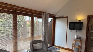 A hotel room with a bed, a chair, a small table, a TV, and a bathroom visible through an open door. - Whortleberry Studio B&B (Minehead)