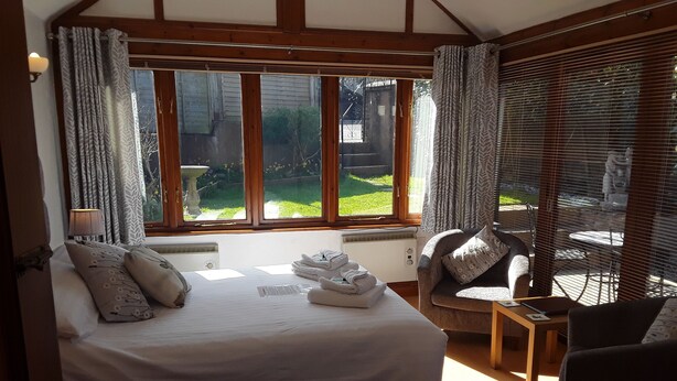 A bedroom with a large bed, a chair, a small table, and a window with curtains. - Whortleberry Studio B&B (Minehead)