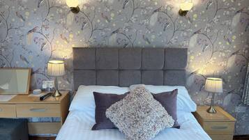 A neatly made bed with a floral-patterned pillow, two bedside lamps, and a wall with a floral wallpaper design.
