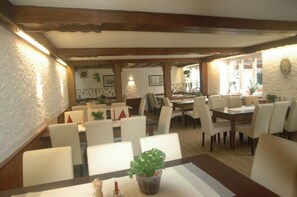 A restaurant with multiple dining tables and chairs, wooden beams on the ceiling, and potted plants on the tables. - Hotel Gasthof Schäffler (Sonthofen)