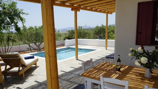 Ein Außenpoolbereich mit Holz-Pergolen, Liegestühlen und einem Tisch mit Weingläsern.