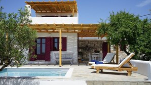 Ein Poolbereich mit Pergola, Liegestühlen und einer Steintreppe, die zu einem Gebäude mit roten Fensterläden führt.