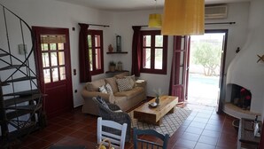 Ein gemütliches Wohnzimmer mit einer Couch, einem Holztisch und einem Korbstuhl. Auf dem Tisch steht ein Korb voller Früchte.